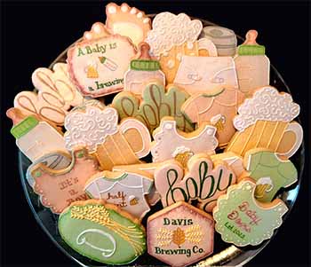 Baby shower cookie tray: Baby bottles, bibs, diaper, onsies, and beer.