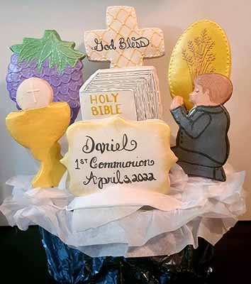 First communion cookie bouquet: Bible, cross, grapes, wheat, chalice with communion wafer, and boy kneeling.